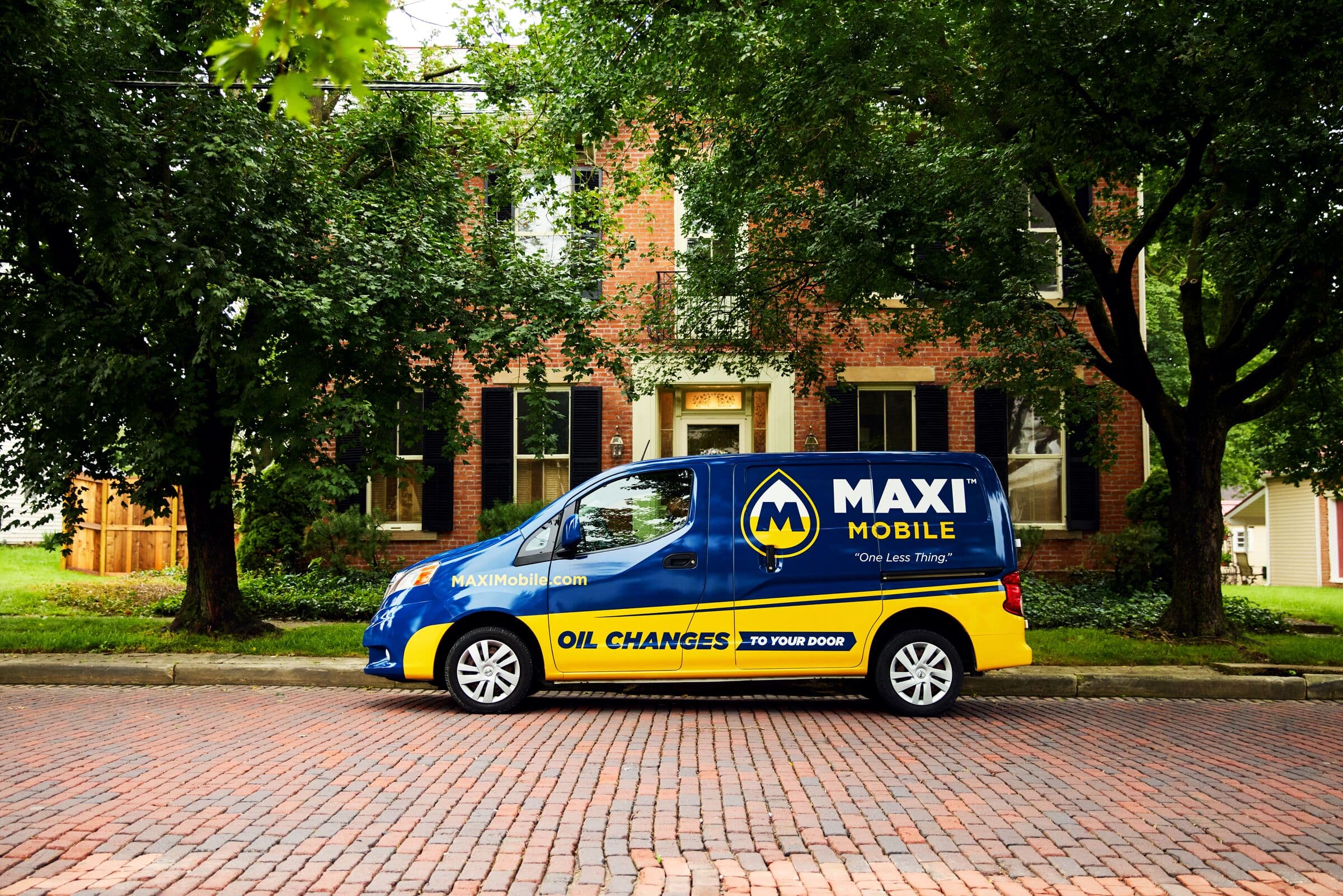 A MAXI Mobile service van parked on a tree-lined brick street