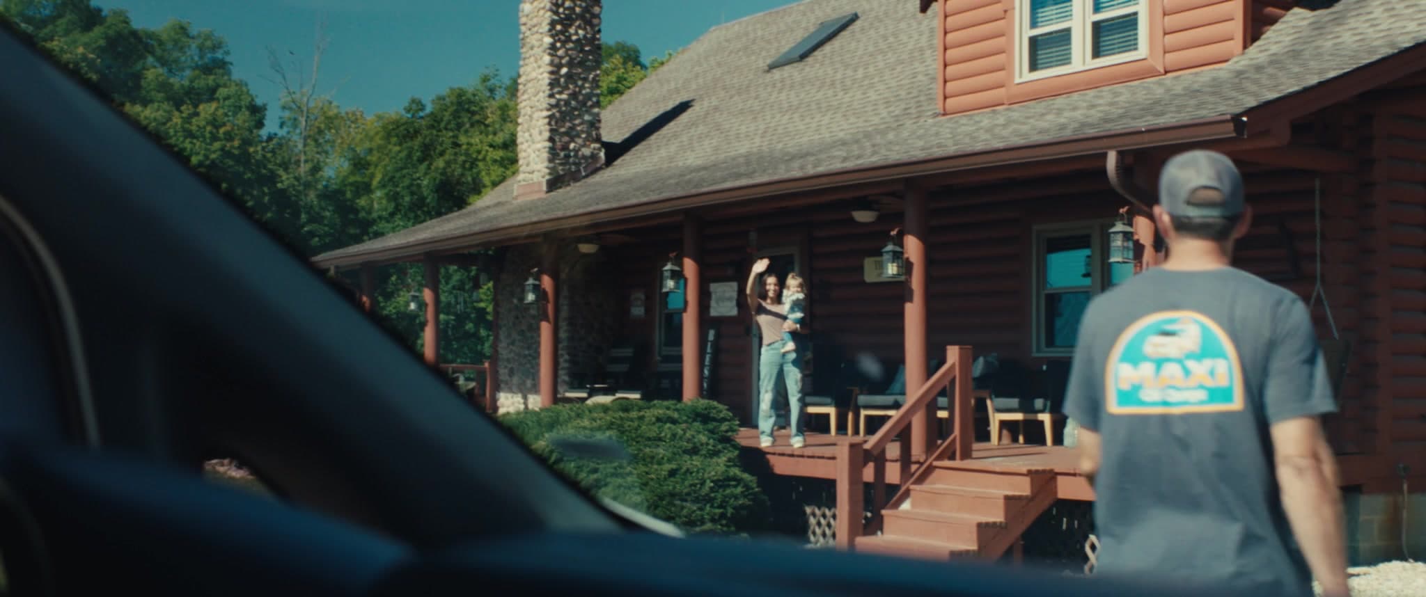 A family waves from their porch as a MAXI technician walks up to service the car
