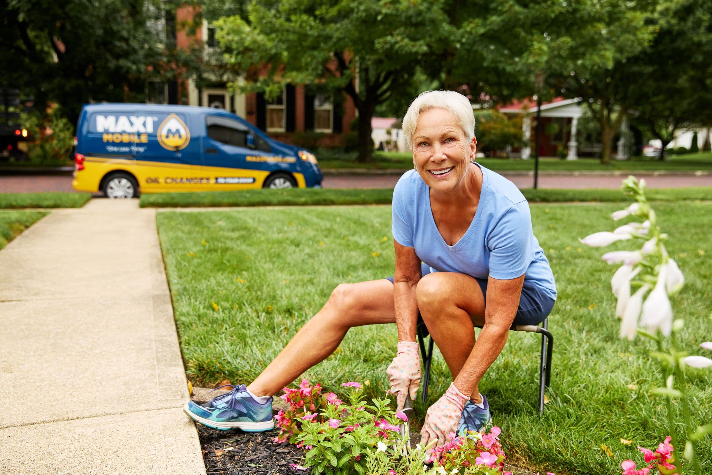 A homeowner gardening in her front yard while a MAXI Mobile van is parked at the curb
