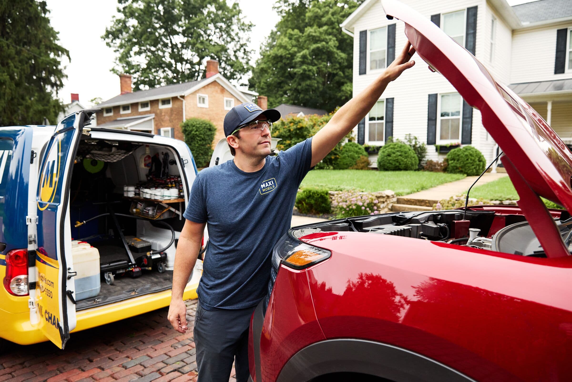 A MAXI technician opening the hood of a customer's SUV beside the service van