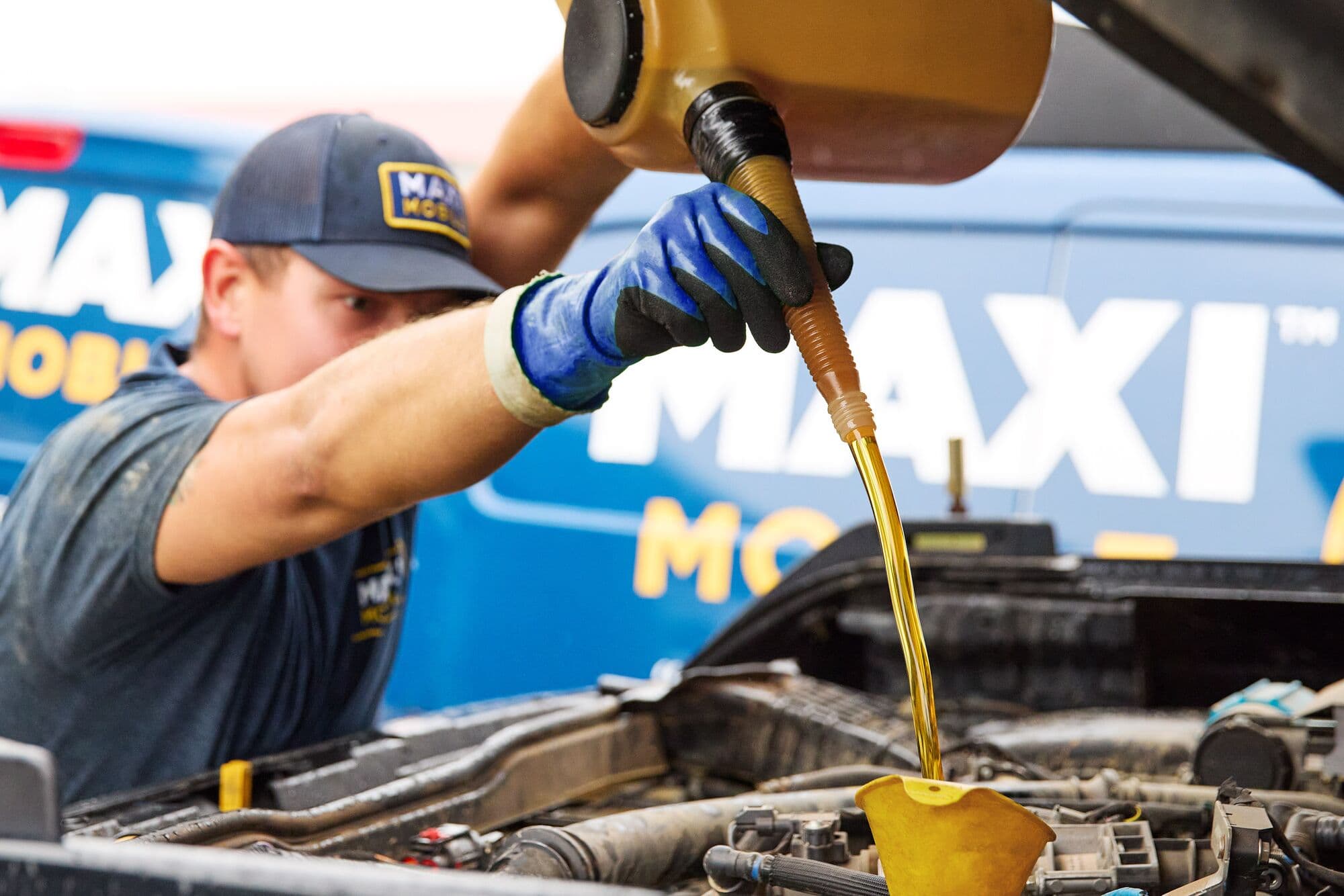 A MAXI Mobile technician pouring full-synthetic oil into an engine beside a branded van